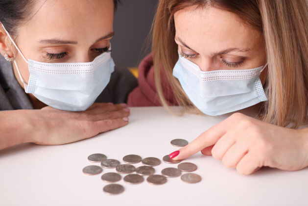 商业两个戴着医用防护面具的女人在看硬币表.商务在冠状病毒大流行中妇女衰退破产