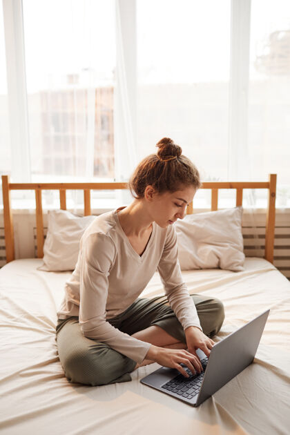 看坐在床上用笔记本电脑打字的年轻女子她在家的卧室里上网工作放松在家工作美容