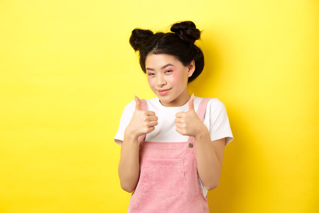 青少年可爱的亚洲少女 美丽的妆容 竖起大拇指 微笑着 赞美你 激励你 赞美你 站在黄色的地面上高兴崇拜魅力提供