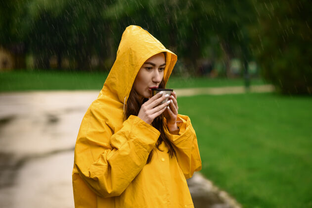 公园雨衣女子在夏日公园喝热茶一天一个人女人穿着雨衣走在小路上 雨天在巷子里徒步旅行户外森林