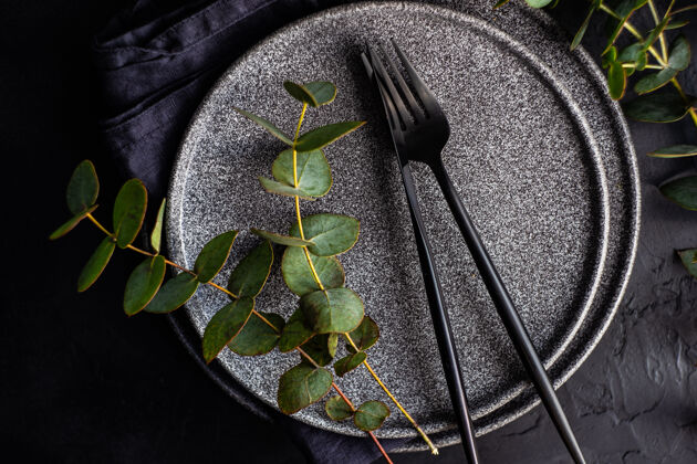 餐具黑色的石头器皿 黑色的餐具 放在用新鲜的绿色桉树叶装饰的黑色水泥桌上餐具春天生的