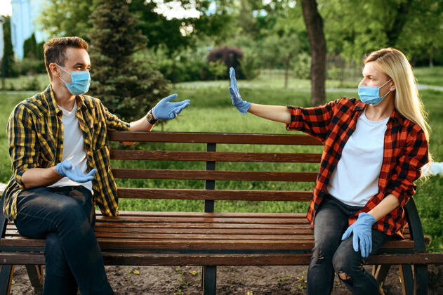 大流行戴着面具和手套坐在公园长椅上的年轻情侣 隔离浪漫会议期间流行 保健和保护 流行的生活方式感染散步疾病