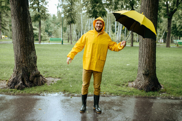 森林风雨交加的夏日公园里打着伞的男人白天男性穿着雨衣和胶靴的人 巷子里天气潮湿自然家伙户外