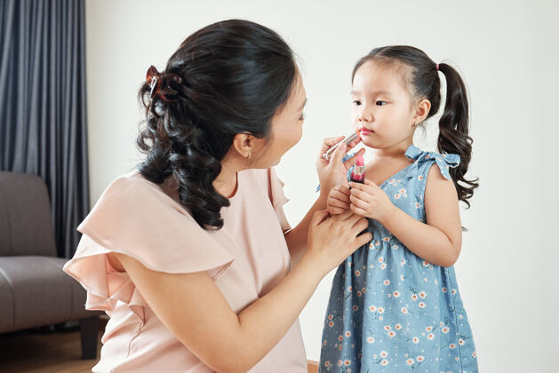 深情微笑的越南女人在她的小女儿的嘴唇上涂上浅粉色的润唇膏人女人爱