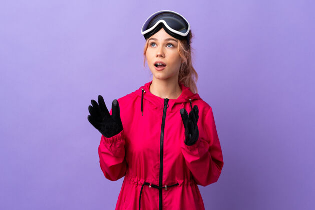 年轻滑雪女孩戴着滑雪板眼镜 脸上孤立的紫色带着惊喜的表情年轻积极假期