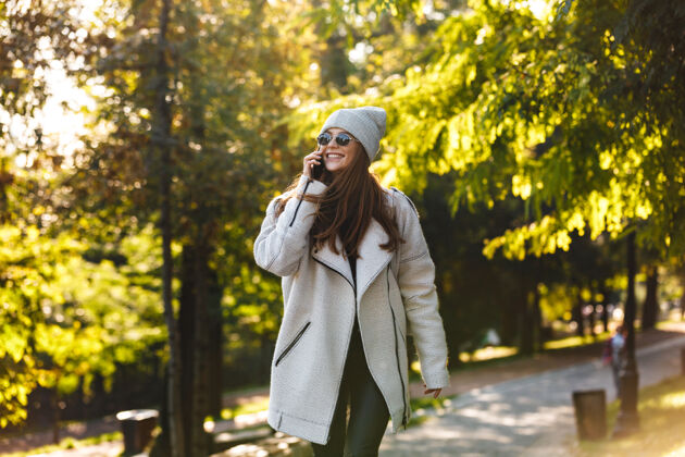 移动穿着秋衣戴秋帽的美丽年轻女子 在户外散步 讲着手机女士成人通信