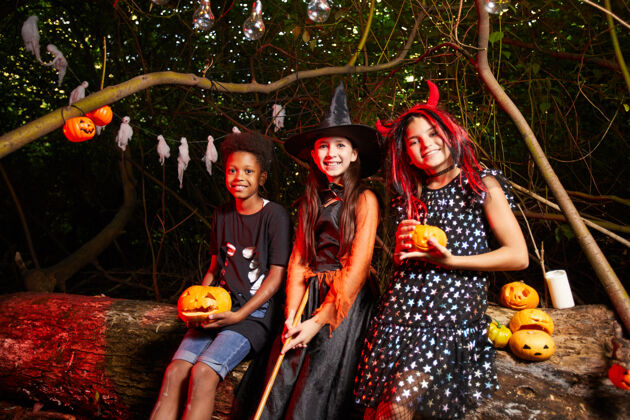女巫一群穿着盛装的朋友在派对上喝着南瓜杯里的果汁 对着镜头微笑夜晚庆祝服装