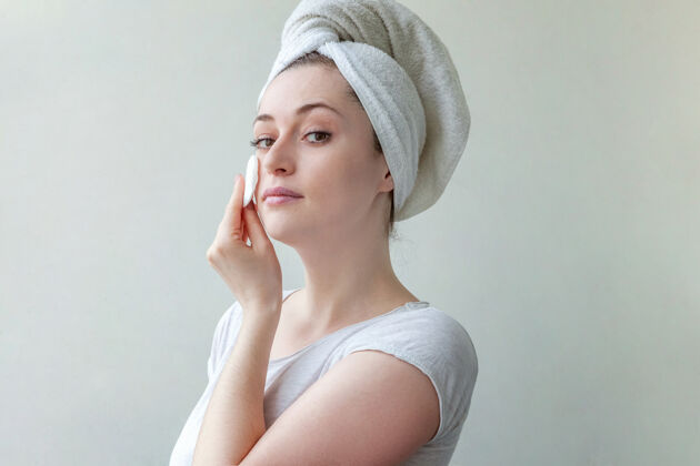洗头上戴着毛巾的微笑女人的美丽肖像 柔软健康的皮肤 用隔离在白色背景上的化妆棉卸妆化妆品应用女性