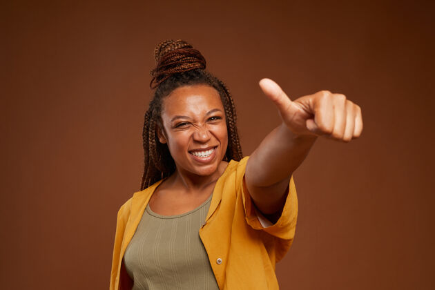 自信在棕色背景下 非洲年轻女子微笑着向镜头竖起大拇指的肖像无忧无虑享受竖起大拇指