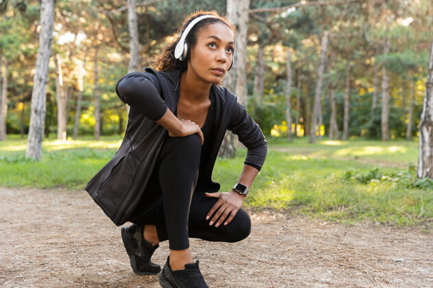 女运动员20多岁的迷人女运动员穿着黑色运动服蹲着 在绿色公园里奔跑运动服户外女人