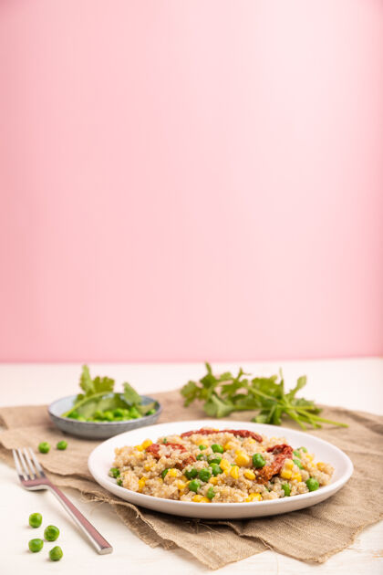 种子奎奴亚藜麦片粥 青豆 玉米和干西红柿放在白色和淡粉色表面和亚麻织物的陶瓷盘子上餐巾纸复制空间料理