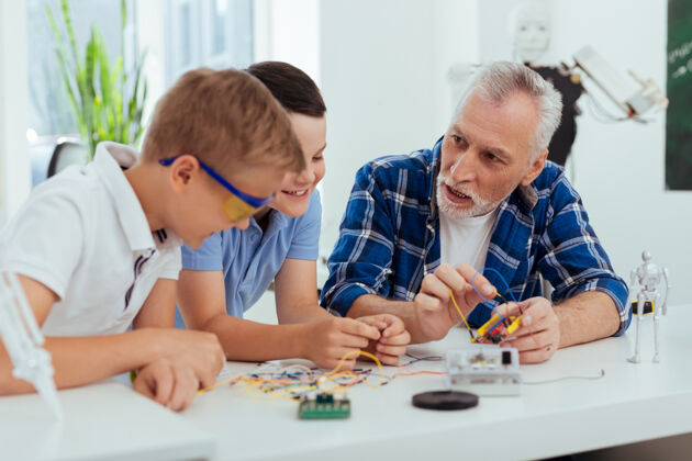 祖父新技能漂亮聪明的男人一边看着他的孙子 一边教他们如何制造机器人社会保障老人家庭