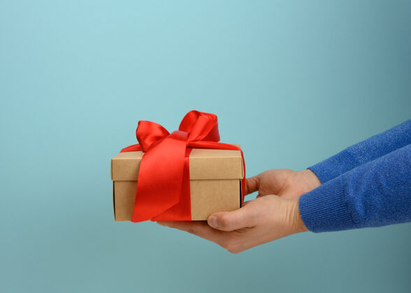 庆祝女的手拿着一个用红丝带绑着的方形盒子 惊喜包装季节购物