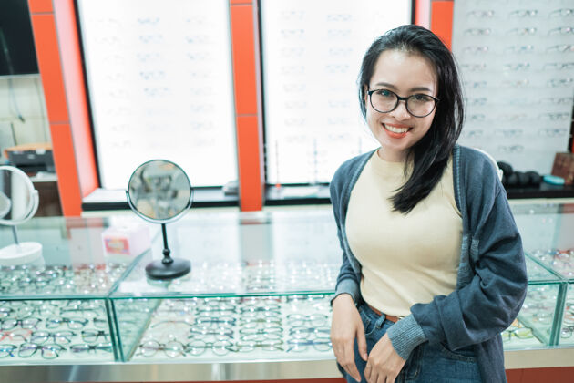 许多一个美丽的女人戴着她选择的眼镜 在一家眼科诊所的眼镜橱窗前摆姿势护理眼睛挑选