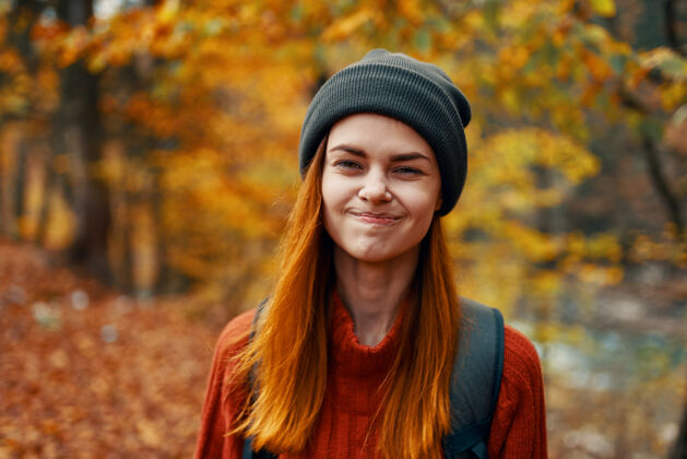 成人一个穿着帽子毛衣 背着背包的美丽女人的肖像在秋天的森林里发现年轻人女人