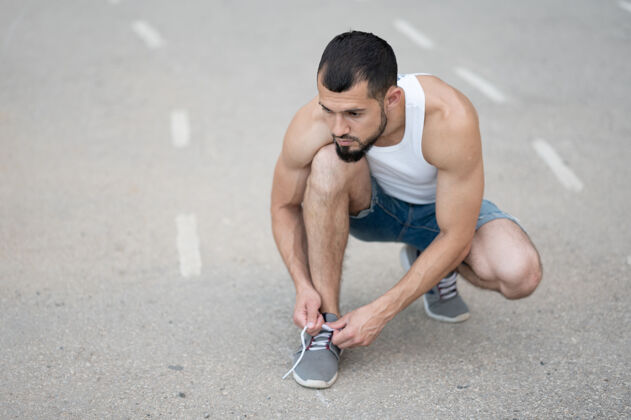 鞋一个爱运动的男人在街上跑步前把鞋带系在运动鞋上赛车花边跑步