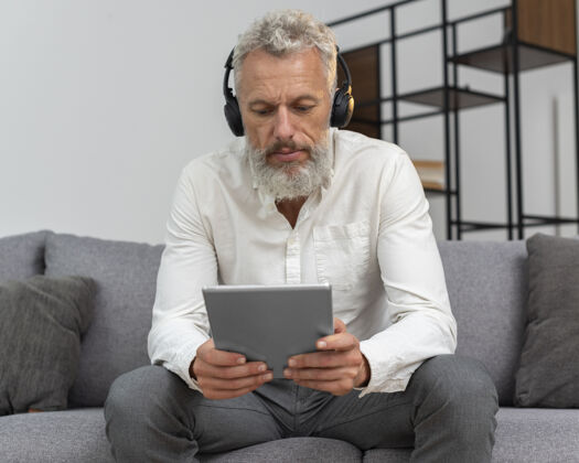 耳机家里的老人在沙发上用平板电脑和耳机设备老年人老年人