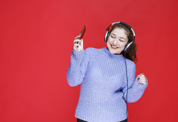 人类戴着耳机的女孩在她的智能手机上放音乐 享受着它设备年轻年轻人