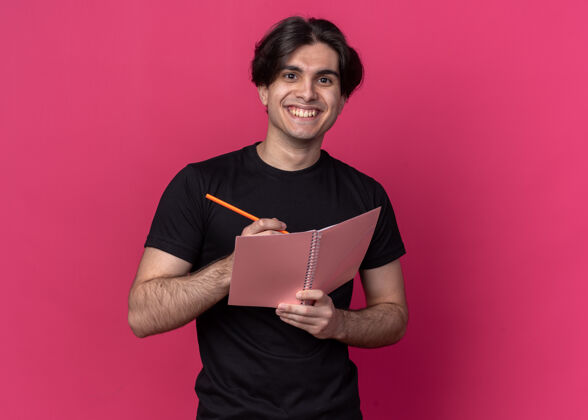 男人面带微笑的年轻帅哥穿着黑色t恤在粉色墙上的笔记本上写着什么等等人表情