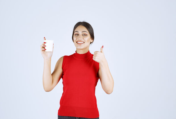 模特穿红衬衫的女孩在喝咖啡 并表现出积极的迹象美味女性员工