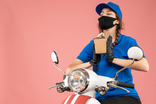 黑色正面图是戴着黑色医用面罩和手套的女快递员 手拿桃色背景的小盒子背景技术设备