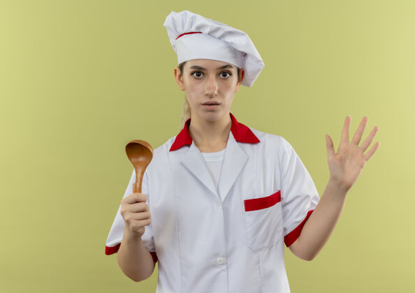 制服年轻漂亮的厨师穿着厨师制服 手里拿着勺子 空荡荡的手被隔离在绿色的墙上厨师年轻显示