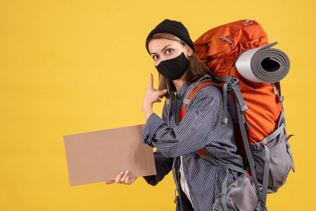 面具带着黑色面具和背包的旅行女孩拿着纸板指着后面成人广播通讯