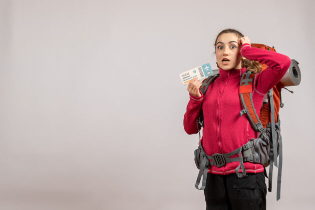 大迷惑不解的年轻旅行者背着大背包 举着灰色的旅行票成人模型背包