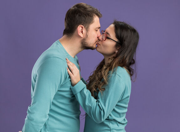 女人身着蓝色休闲服的年轻漂亮夫妇站在紫色的墙上 热吻着相爱的男人和女人站立情侣男人