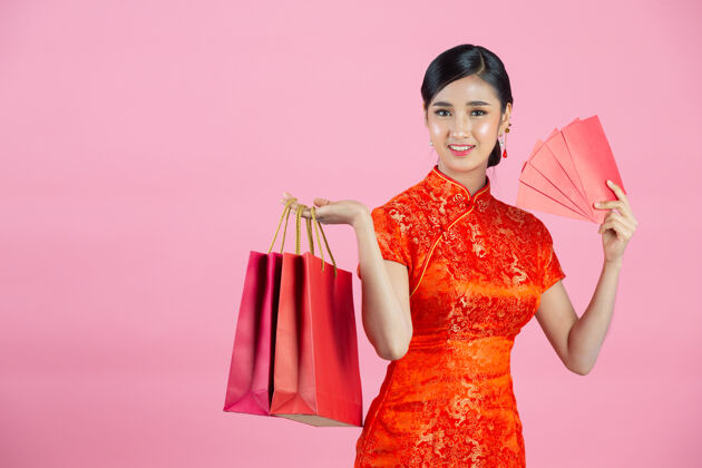 新美丽的亚洲女人快乐的微笑和购物在中国新年的粉红色背景女性展示女人