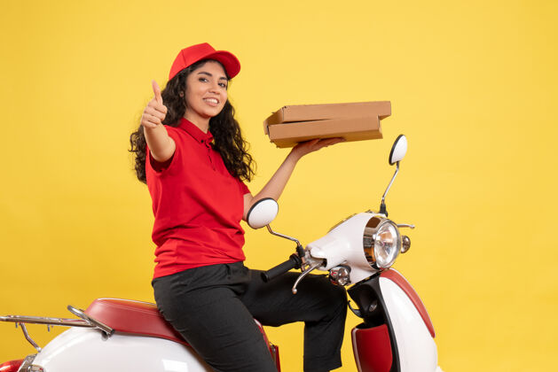 成人正面图骑自行车的女快递员拿着黄色背景的披萨盒工作服工作服工人送货工作人坐着制服