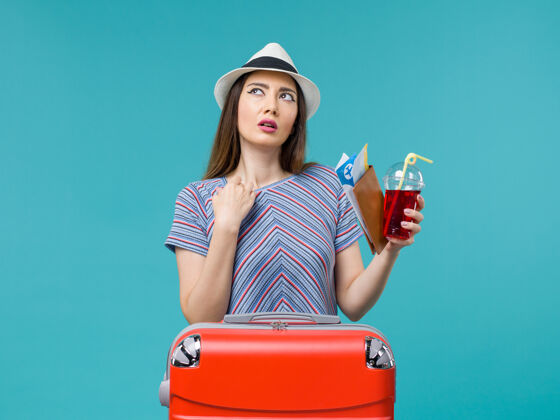 成人前景度假中的女人拿着果汁和机票在蓝色背景的海上避暑女飞机上旅行举行肖像票