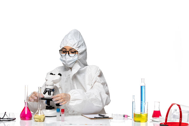 研究前视图穿着特殊防护服的年轻女化学家正在用显微镜观察白色背景的化学实验室病毒外套防护实验室外套