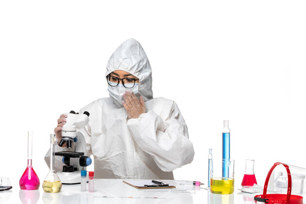 实验室外套前视图年轻的女化学家穿着特殊的防护服在显微镜下用浅白色背景病毒实验室冠状病毒健康化学医学使用套装