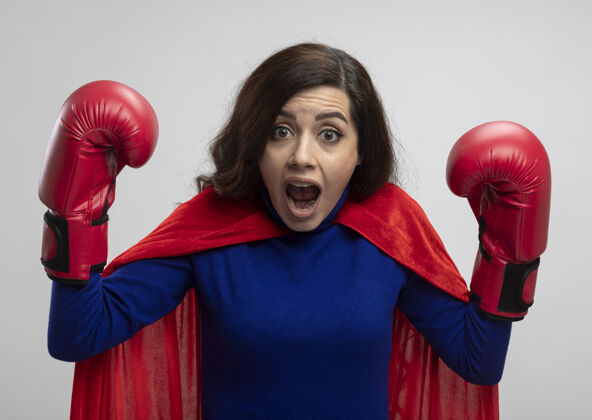 拳击焦急的高加索超级英雄女孩穿着红色斗篷 戴着拳击手套站着手套举起手