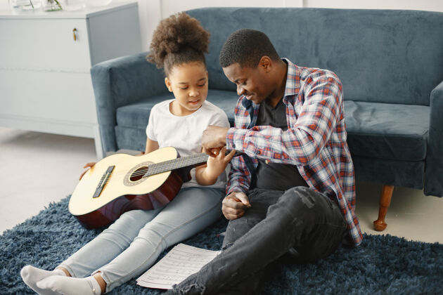 舒适父亲带着女儿坐在沙发上女孩拿着吉他学吉他情感乐趣大笑