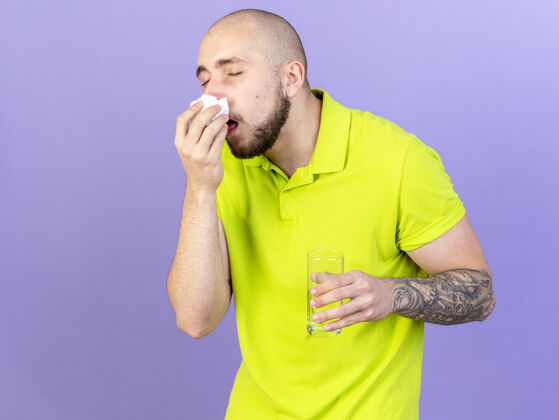 疾病苍白的年轻白人病人用纸巾擦鼻子 拿着一杯紫色的水年轻紫色水