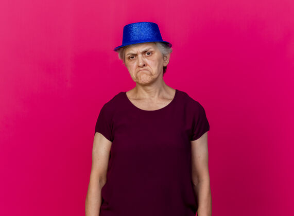 站着戴着聚会帽的未出嫁的老妇人站在粉红色的地板上聚会不愉快女人