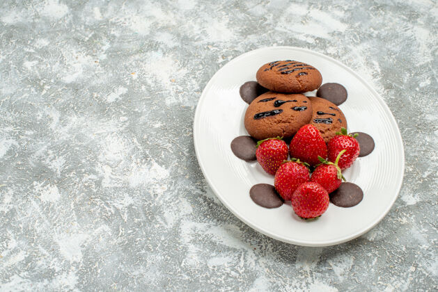 研磨底视图巧克力饼干草莓和圆形巧克力的白色椭圆形板在右侧的灰白色背景壁板甜点右