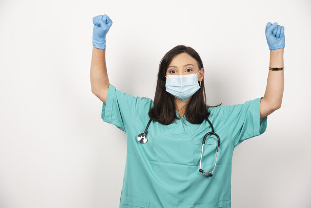 站立戴着面具的女医生在白色背景上展示她的拳头高质量的照片保健医疗健康