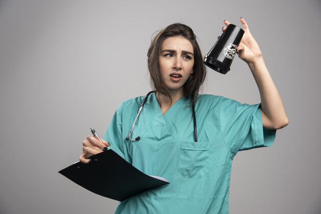 剪贴板疲惫的医生拿着杯子和剪贴板在灰色背景上高质量的照片健康医生诊所