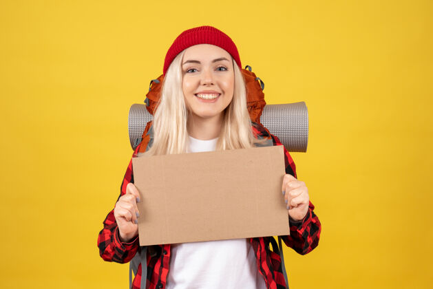帽子正面图年轻的旅行女孩戴着红帽子拿着纸板站在黄色的墙上女士站着硬纸板