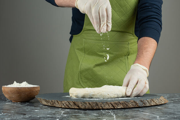准备男人戴着手套在大理石桌上做面团面包房小麦人