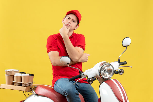 背景前视图是一个穿着红色上衣 戴着帽子 在黄色背景下传递命令的年轻人坐着年轻人摩托车