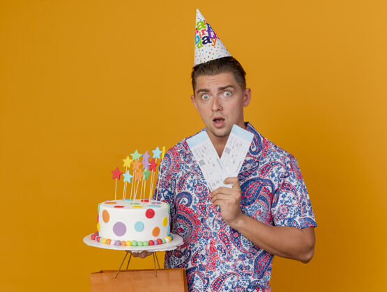 聚会惊喜的年轻人戴着生日帽拿着礼物袋蛋糕和门票孤立在橙色年轻蛋糕穿
