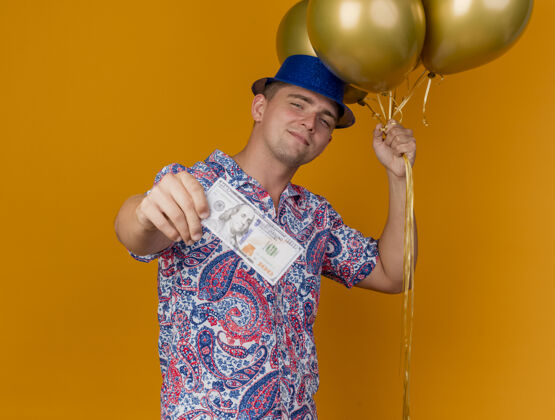 现金高兴的年轻人戴着蓝帽子 拿着气球 拿着现金孤立在橙色帽子橙色蓝色