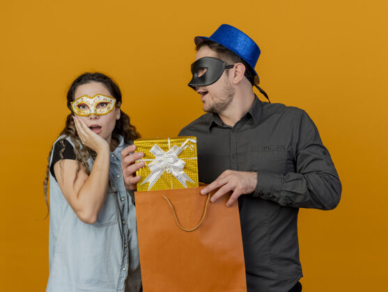 惊喜年轻的派对情侣戴着化装眼罩的家伙送礼物惊喜的女孩孤立在橙色穿礼物派对