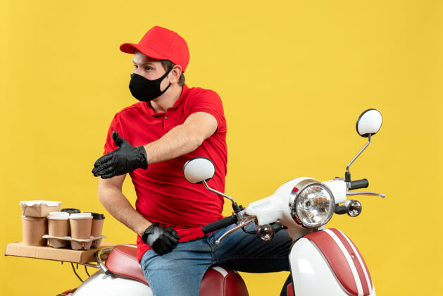 运动俯视图：忙碌的年轻人穿着红色上衣 戴着帽子 戴着手套 戴着医用口罩 坐在踏板车上欢迎某人运动车辆手套