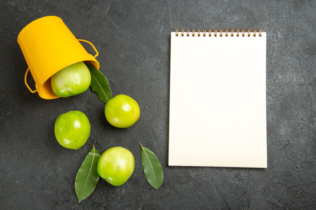 深色顶视图绿色的西红柿湾树叶翻转黄色的桶和一个笔记本在黑暗的背景食物桶有机