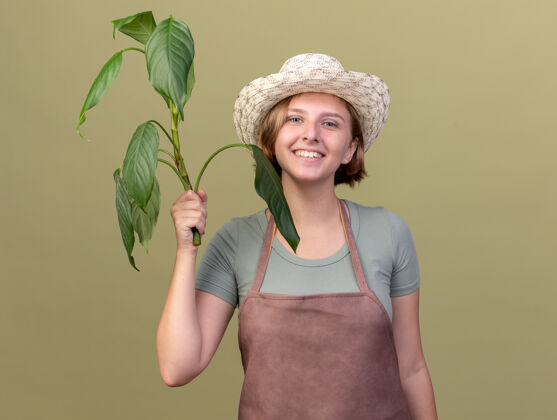 帽子微笑着的年轻的斯拉夫女园丁戴着园艺帽拿着橄榄绿上的植物园艺花园斯拉夫